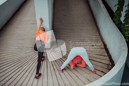 Image of Two women warming up together and preparing for a morning run in an urban environment. Selective focus