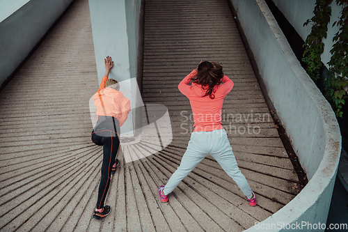 Image of Two women warming up together and preparing for a morning run in an urban environment. Selective focus