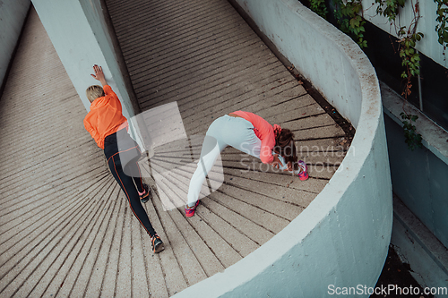 Image of Two women warming up together and preparing for a morning run in an urban environment. Selective focus