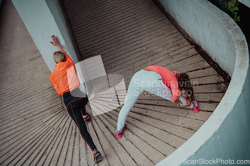 Image of Two women warming up together and preparing for a morning run in an urban environment. Selective focus