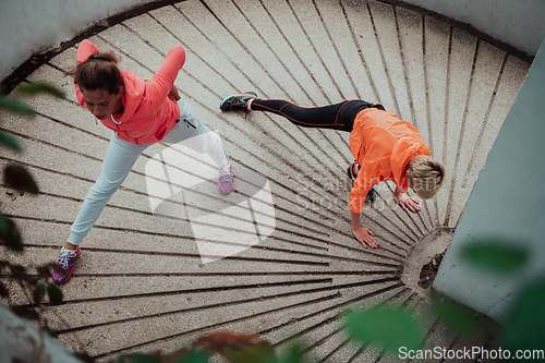 Image of Two women warming up together and preparing for a morning run in an urban environment. Selective focus