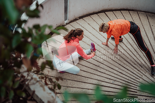 Image of Two women warming up together and preparing for a morning run in an urban environment. Selective focus