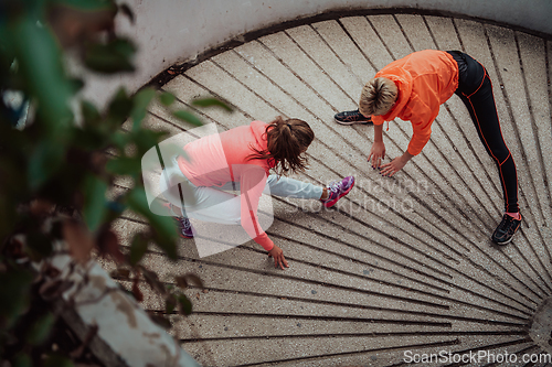 Image of Two women warming up together and preparing for a morning run in an urban environment. Selective focus