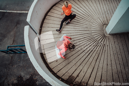 Image of Two women warming up together and preparing for a morning run in an urban environment. Selective focus