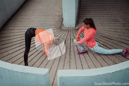 Image of Two women warming up together and preparing for a morning run in an urban environment. Selective focus