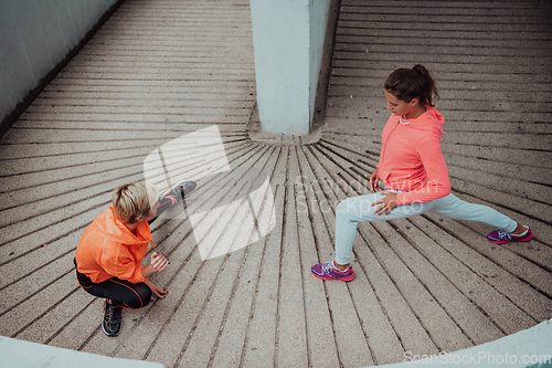 Image of Two women warming up together and preparing for a morning run in an urban environment. Selective focus