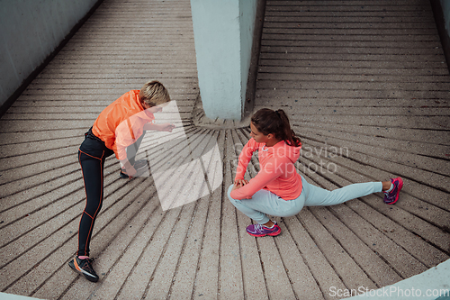 Image of Two women warming up together and preparing for a morning run in an urban environment. Selective focus