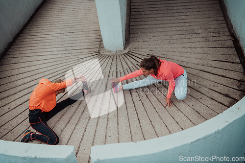 Image of Two women warming up together and preparing for a morning run in an urban environment. Selective focus