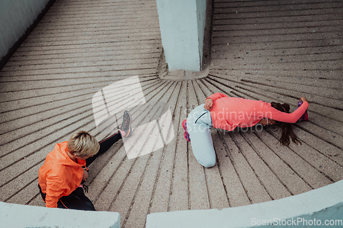 Image of Two women warming up together and preparing for a morning run in an urban environment. Selective focus