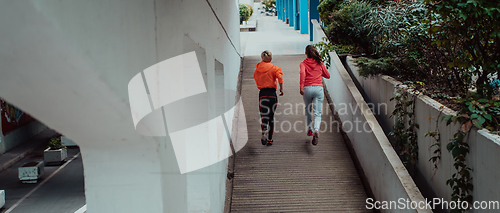 Image of Two women in sports clothes running in a modern urban environment. The concept of a sporty and healthy lifestyle