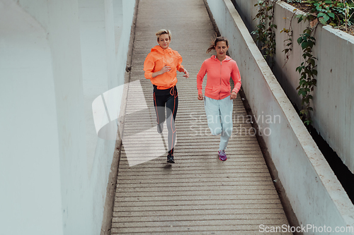 Image of Two women in sports clothes running in a modern urban environment. The concept of a sporty and healthy lifestyle