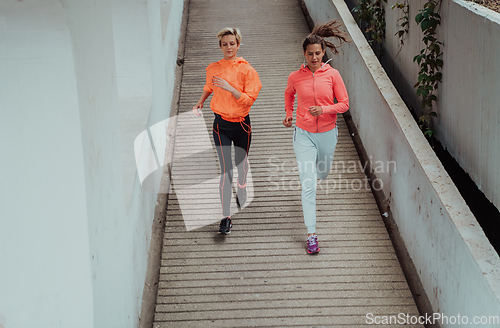 Image of Two women in sports clothes running in a modern urban environment. The concept of a sporty and healthy lifestyle