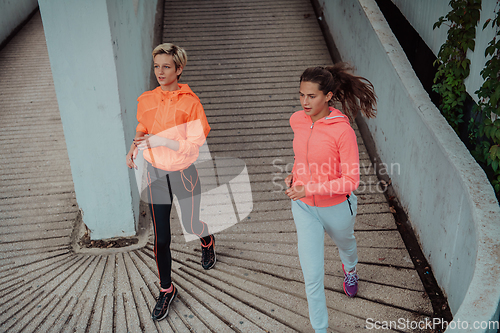 Image of Two women in sports clothes running in a modern urban environment. The concept of a sporty and healthy lifestyle