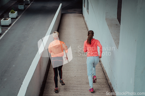 Image of Two women in sports clothes running in a modern urban environment. The concept of a sporty and healthy lifestyle