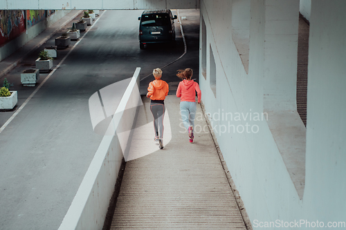 Image of Two women in sports clothes running in a modern urban environment. The concept of a sporty and healthy lifestyle