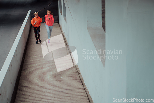 Image of Two women in sports clothes running in a modern urban environment. The concept of a sporty and healthy lifestyle