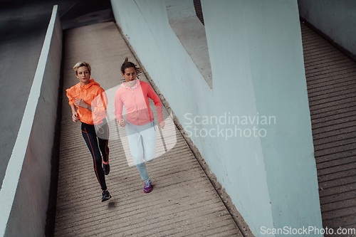 Image of Two women in sports clothes running in a modern urban environment. The concept of a sporty and healthy lifestyle