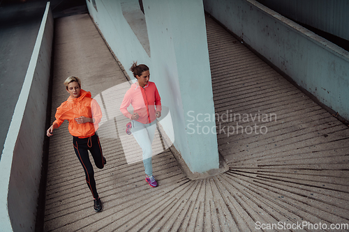 Image of Two women in sports clothes running in a modern urban environment. The concept of a sporty and healthy lifestyle