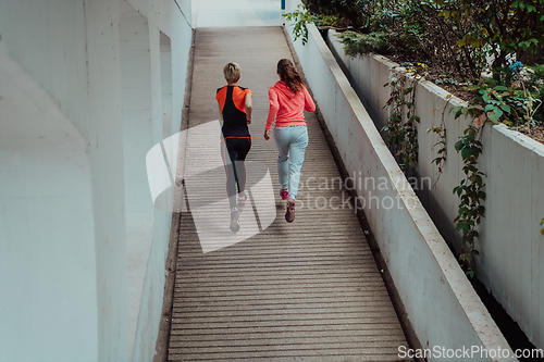 Image of Two women in sports clothes running in a modern urban environment. The concept of a sporty and healthy lifestyle