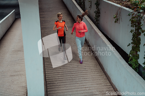 Image of Two women in sports clothes running in a modern urban environment. The concept of a sporty and healthy lifestyle