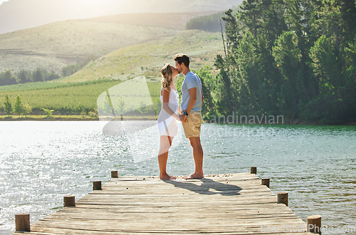 Image of Couple, kissing and holding hands by the lake in romance for love, care and affection together in nature. Man and woman kiss by water on a romantic getaway, summer vacation or date by the lakeside