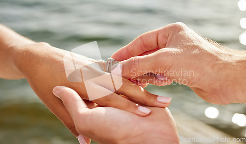 Image of Hands, proposal and engagement ring at lake outdoors for couple, marriage and wedding. Commitment, love and jewelry of woman and man proposing and putting band on finger for trust, care and romance.