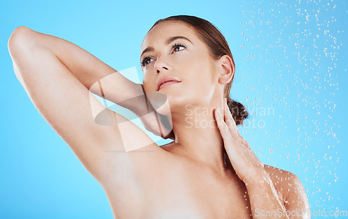 Image of Water drops, shower and woman washing in studio for skincare, wellness and clean body for self care. Face of female aesthetic model with splash for cleaning, hygiene and cosmetics on blue background