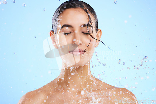 Image of Water splash, beauty and skincare with a woman in studio on a blue background for hygiene or hydration. Relax, wellness and cleaning with an attractive young female in the shower for self care