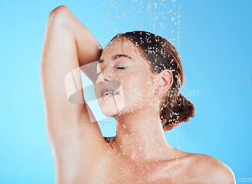 Image of Water, shower and woman cleaning her body as skincare, dermatology and self care isolated in a studio blue background. Aqua, beauty and female model washing her skin for wellness while feeling calm