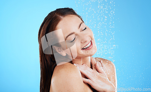 Image of Water drop, shower and happy woman washing her body, skincare and self care isolated in a studio blue background. Aqua, beauty and female model cleaning her skin as wellness feeling calm and relaxed
