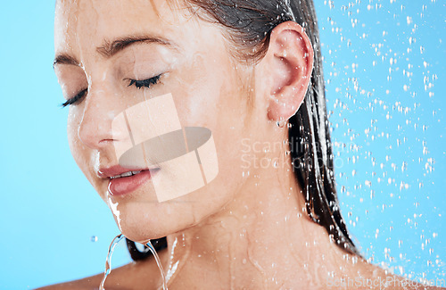 Image of Shower, water and woman face in a studio relax from cleaning and facial skincare. Wellness, splash and beauty routine of female model in bathroom from dermatology and self care with blue background