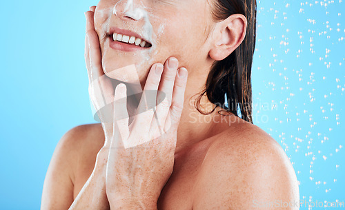 Image of Woman face, wash and shower studio with a young female hands doing skincare and beauty routine. Bathroom, dermatology and facial treatment of a model smile from cleaning and isolated blue background