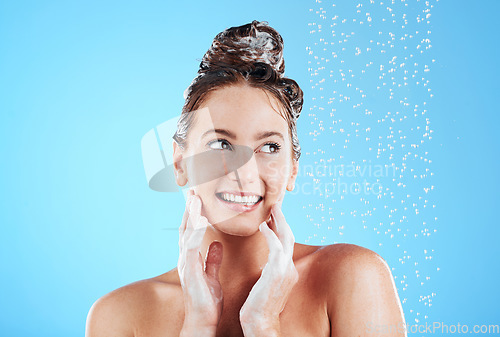 Image of Haircare, shower and woman in a studio with a beauty, wellness and healthy self care routine. Happy, smile and female model washing her hair with shampoo and water while isolated by a blue background