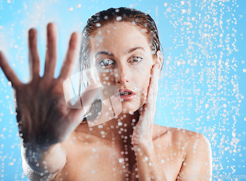 Image of Shower portrait, water drops and woman hand doing skin cleaning, wellness and beauty routine in bathroom. Isolated, blue background and studio with young female doing hair care and dermatology facial