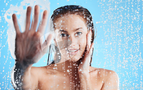 Image of Shower portrait, water drops and woman hand against glass doing skin cleaning and beauty routine. Isolated, blue background and studio with a young female doing hair care and dermatology facial