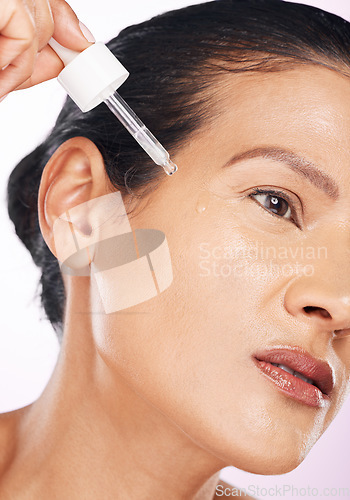 Image of Face, skincare and woman with serum in studio isolated on a purple background. Dermatology, cosmetics and serious mature female model apply hyaluronic acid, retinol or essential oil for anti aging.