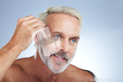 Image of Old man, smile and facial oil for skincare, beauty and grooming, apply serum on face against studio background. Dropper, anti aging cosmetic care with senior male and mockup, hygiene with dermatology