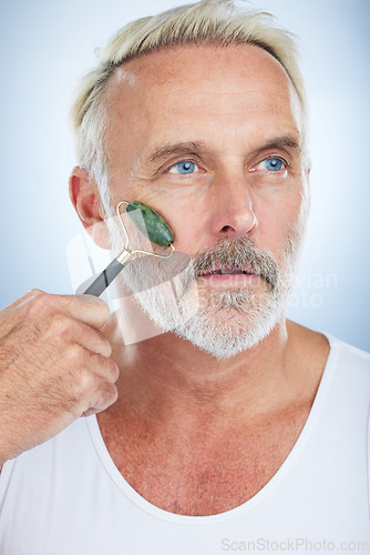 Image of Senior man, jade roller and facial skincare with clean, self care and wellness in studio by white background. Elderly model, face skin massage or beauty with stone product, glow and dermatology detox