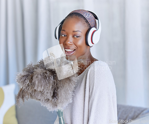 Image of Happy, black woman and cleaning with headphones music, singing and enjoying radio while housekeeping. Smile, duster and an African girl listening to a podcast or audio to clean the living room