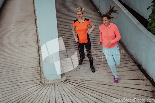 Image of Two women in sports clothes running in a modern urban environment. The concept of a sporty and healthy lifestyle