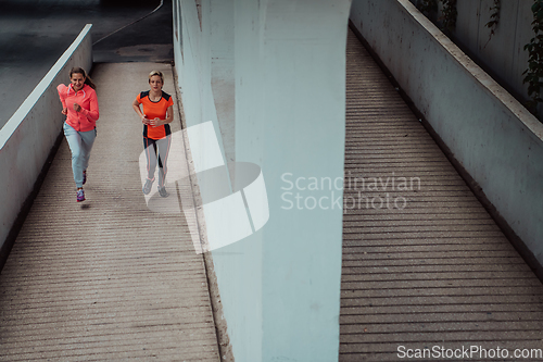 Image of Two women in sports clothes running in a modern urban environment. The concept of a sporty and healthy lifestyle