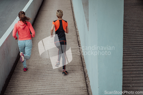 Image of Two women in sports clothes running in a modern urban environment. The concept of a sporty and healthy lifestyle