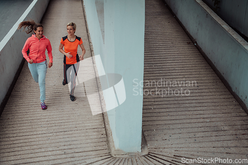 Image of Two women in sports clothes running in a modern urban environment. The concept of a sporty and healthy lifestyle