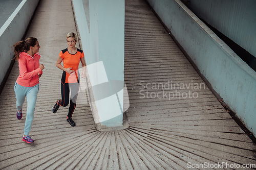 Image of Two women in sports clothes running in a modern urban environment. The concept of a sporty and healthy lifestyle