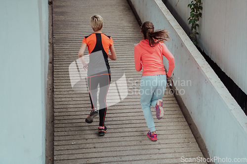 Image of Two women in sports clothes running in a modern urban environment. The concept of a sporty and healthy lifestyle