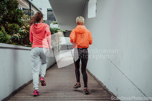 Image of Two women in sports clothes running in a modern urban environment. The concept of a sporty and healthy lifestyle