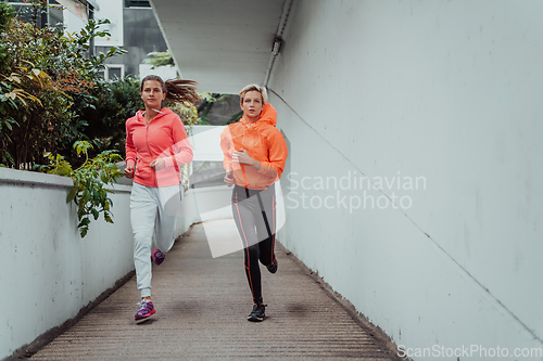 Image of Two women in sports clothes running in a modern urban environment. The concept of a sporty and healthy lifestyle