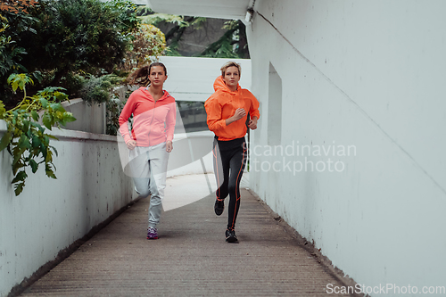 Image of Two women in sports clothes running in a modern urban environment. The concept of a sporty and healthy lifestyle