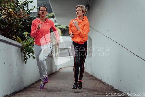 Image of Two women in sports clothes running in a modern urban environment. The concept of a sporty and healthy lifestyle