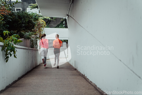 Image of Two women in sports clothes running in a modern urban environment. The concept of a sporty and healthy lifestyle